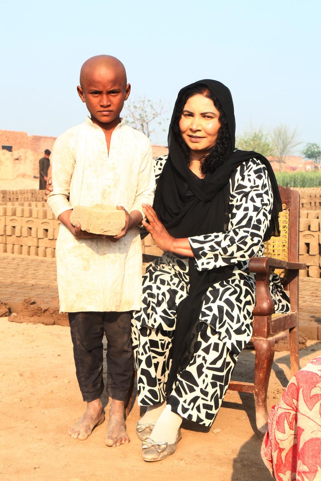 A barefoot boy at the kiln handing a brick to a visiting team member