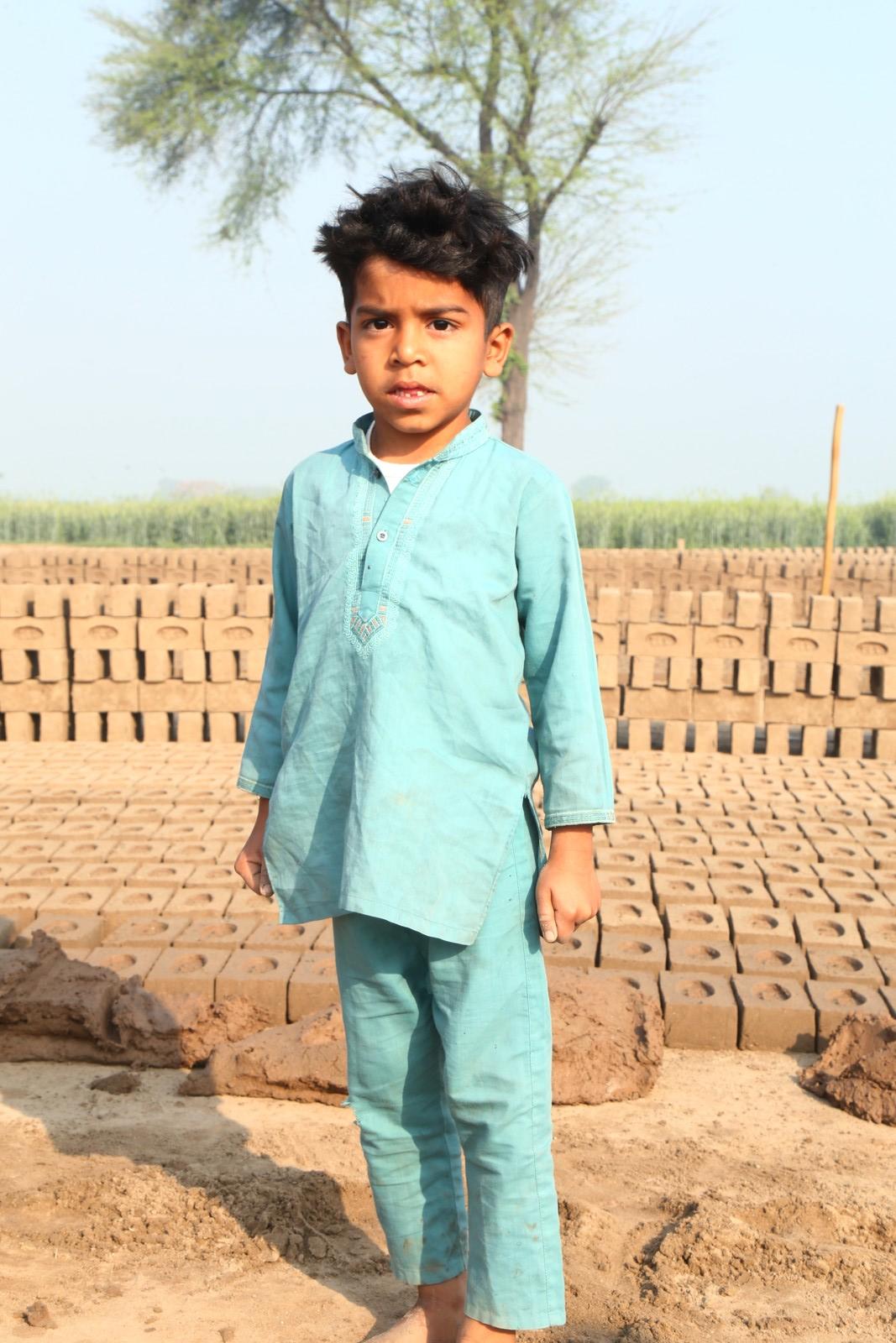 A boy standing beside stacks of drying bricks